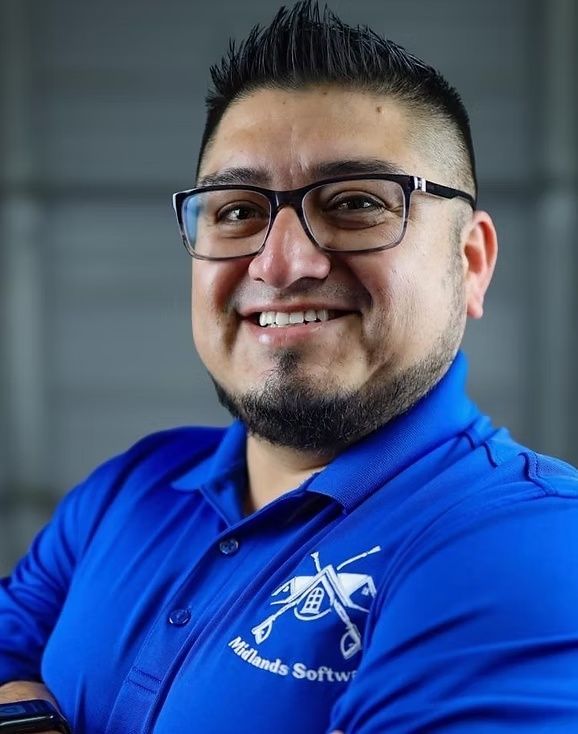 Smiling person in glasses wearing a blue polo shirt with a logo, against a gray background