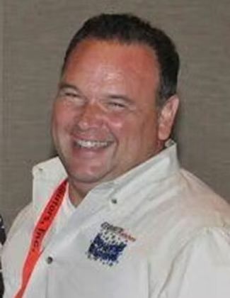 Smiling man in a white shirt with a red lanyard, standing against a plain background.