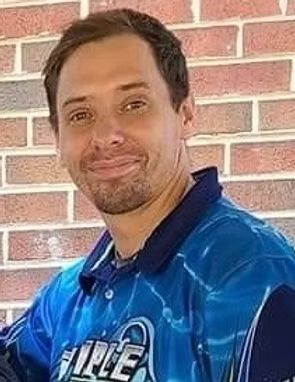 Smiling person in a blue sports jersey standing against a brick wall
