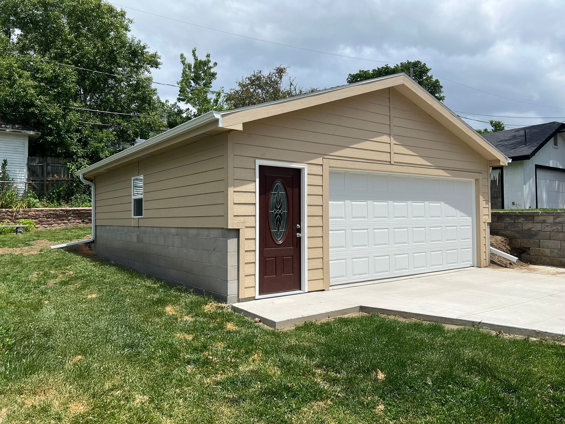 Beige two-story house with green garage door, stone accents, and blue sky.