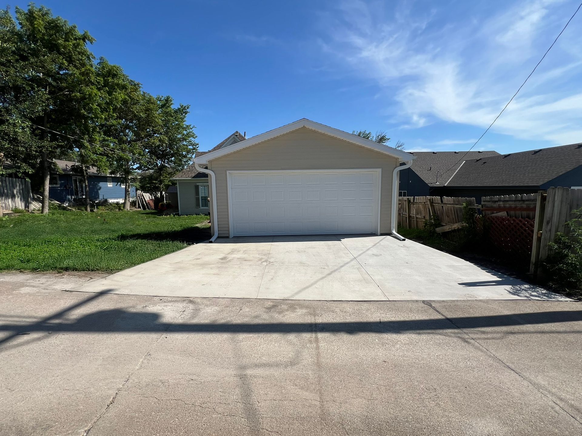 Beige garage door with windows, black hardware, and a pergola above.
