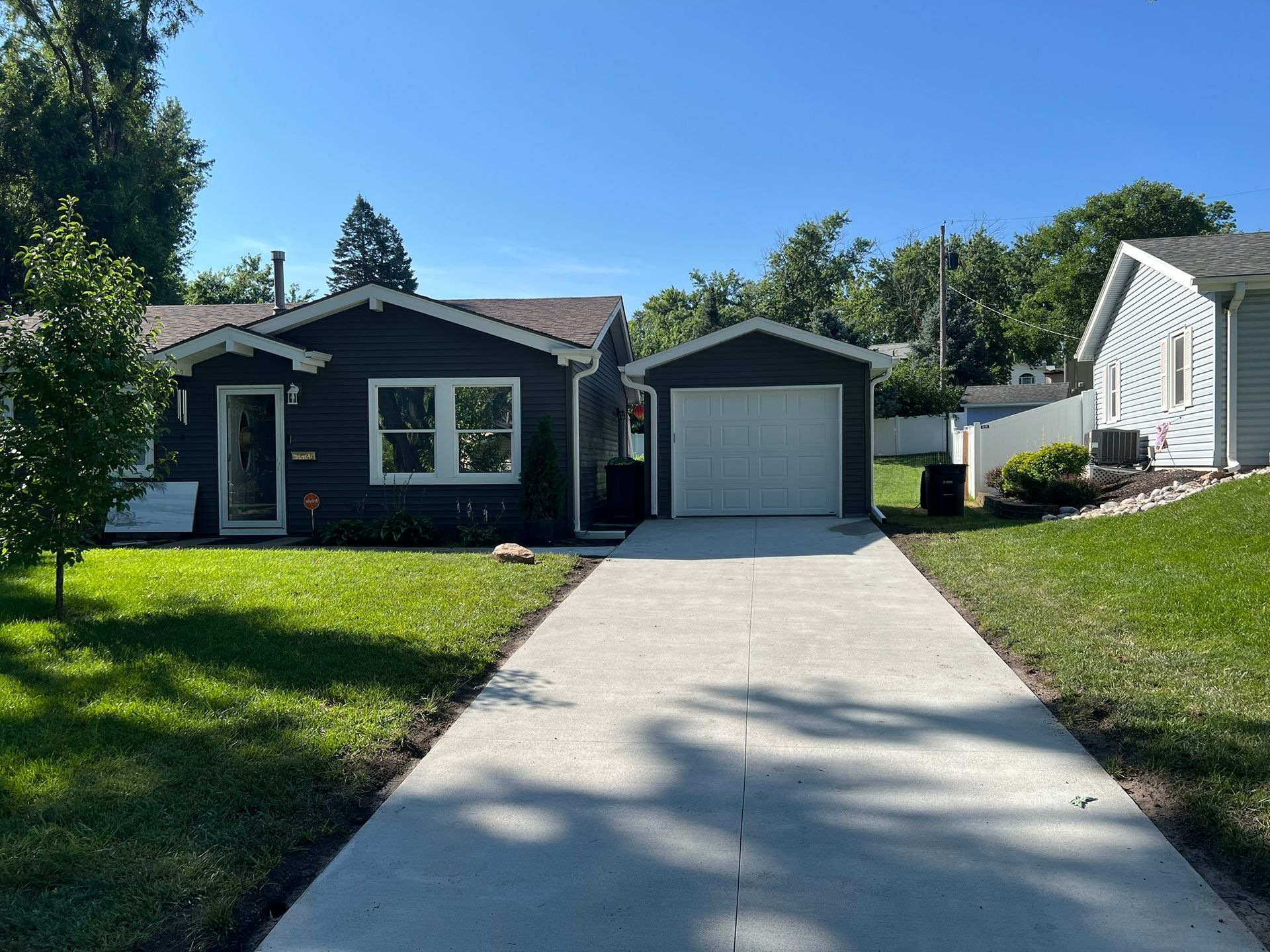 Dark gray garage door with a modern planter and lush greenery.