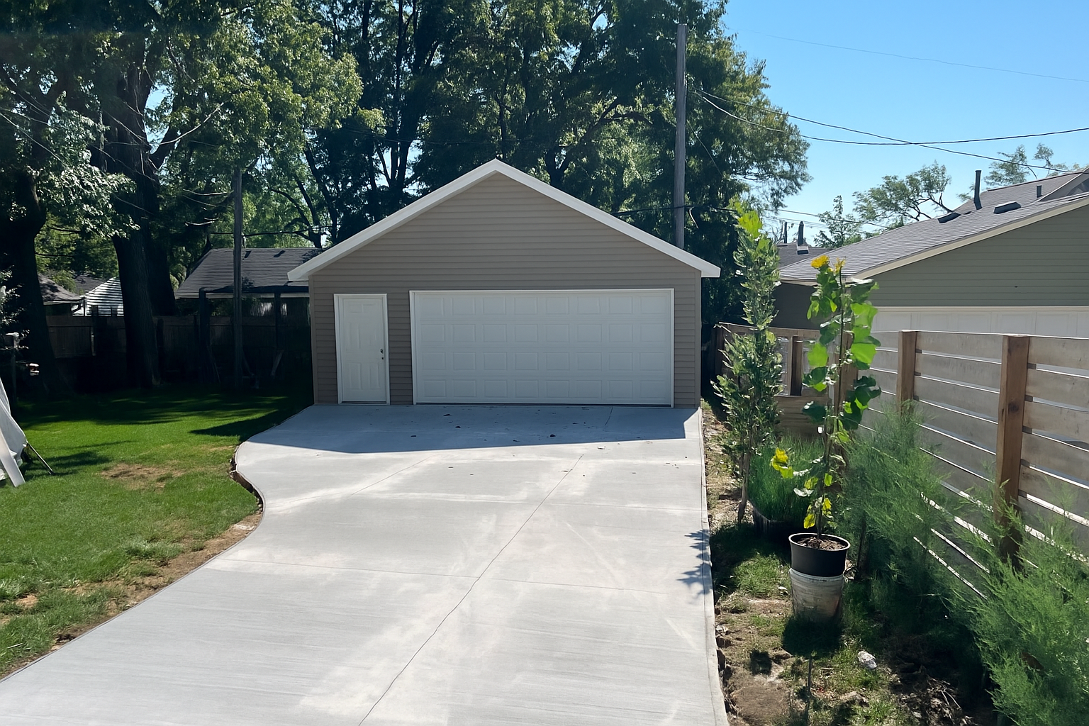 Concrete driveway leading to a two-car garage, tan siding, white door and garage door, greenery.