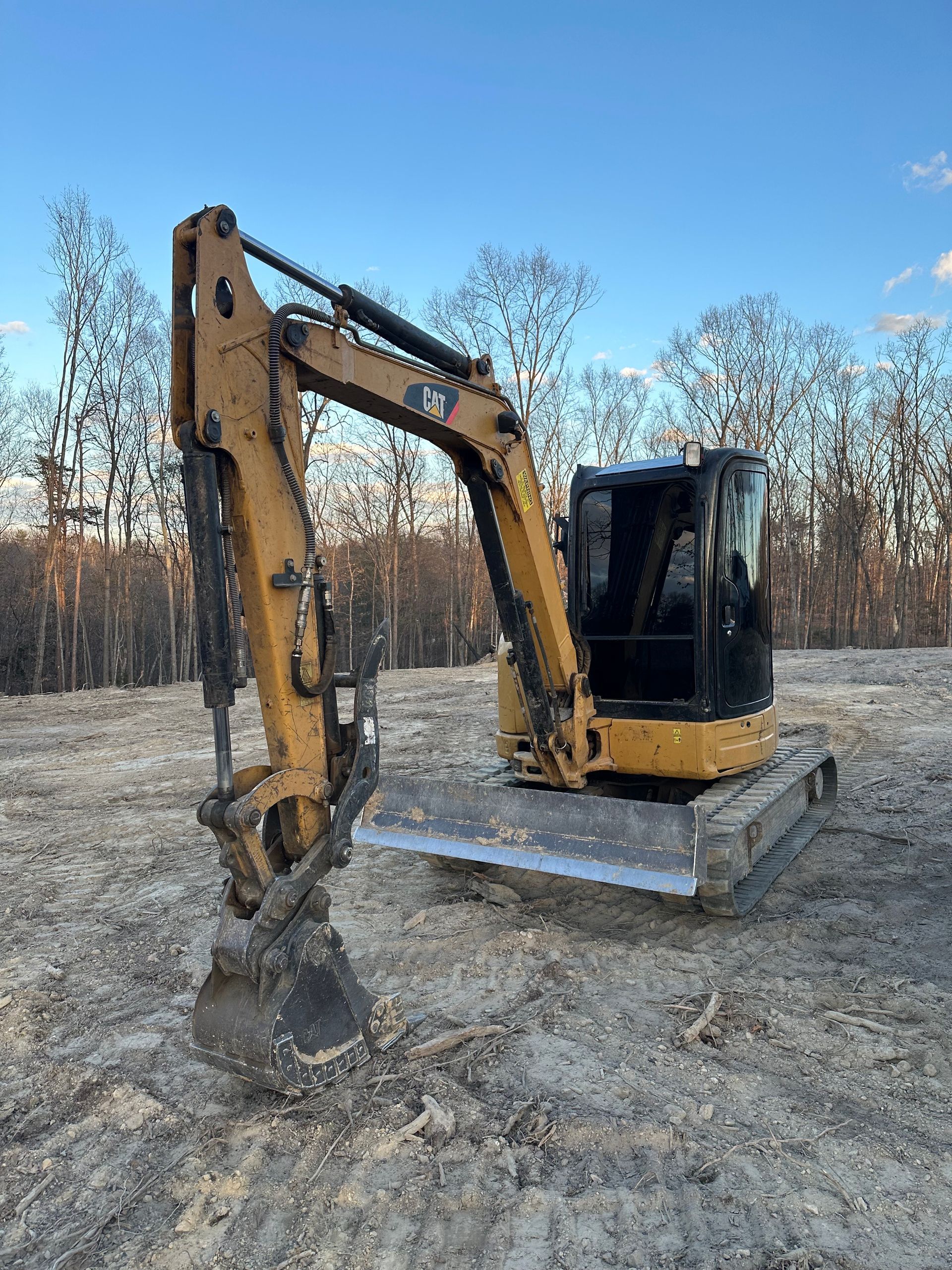 A small excavator is sitting in the middle of a dirt field.