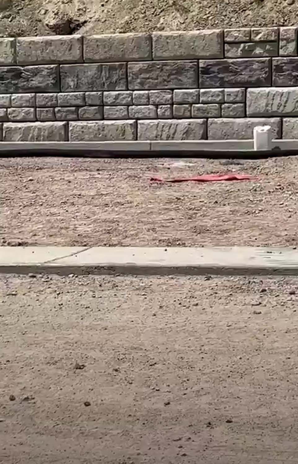 A brick wall is being built on the side of a dirt road.