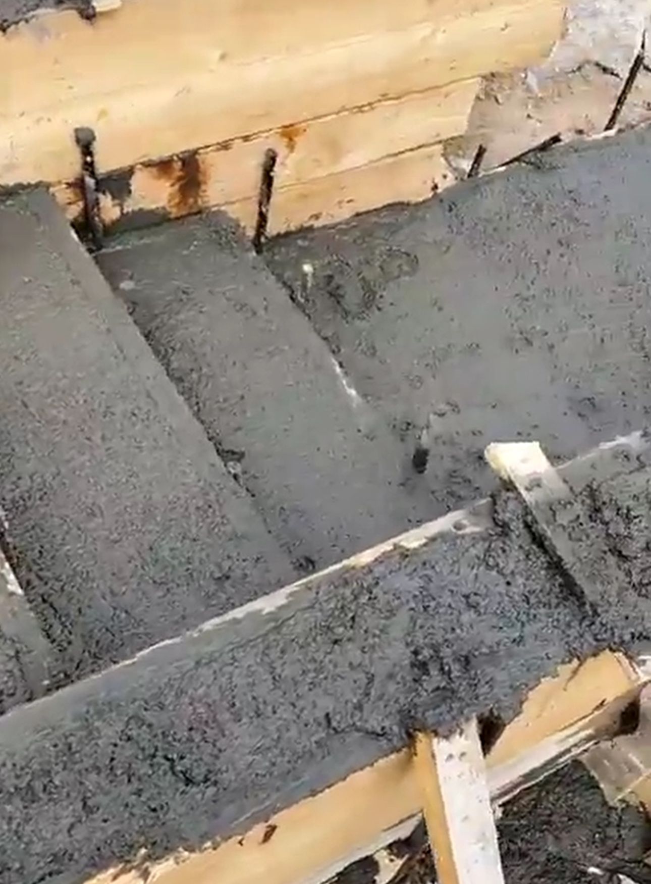 Concrete is being poured into a wooden frame on a construction site.