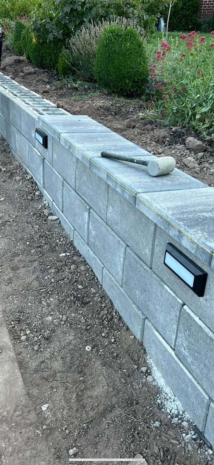 A brick wall is being built in a garden with a hammer on top of it.