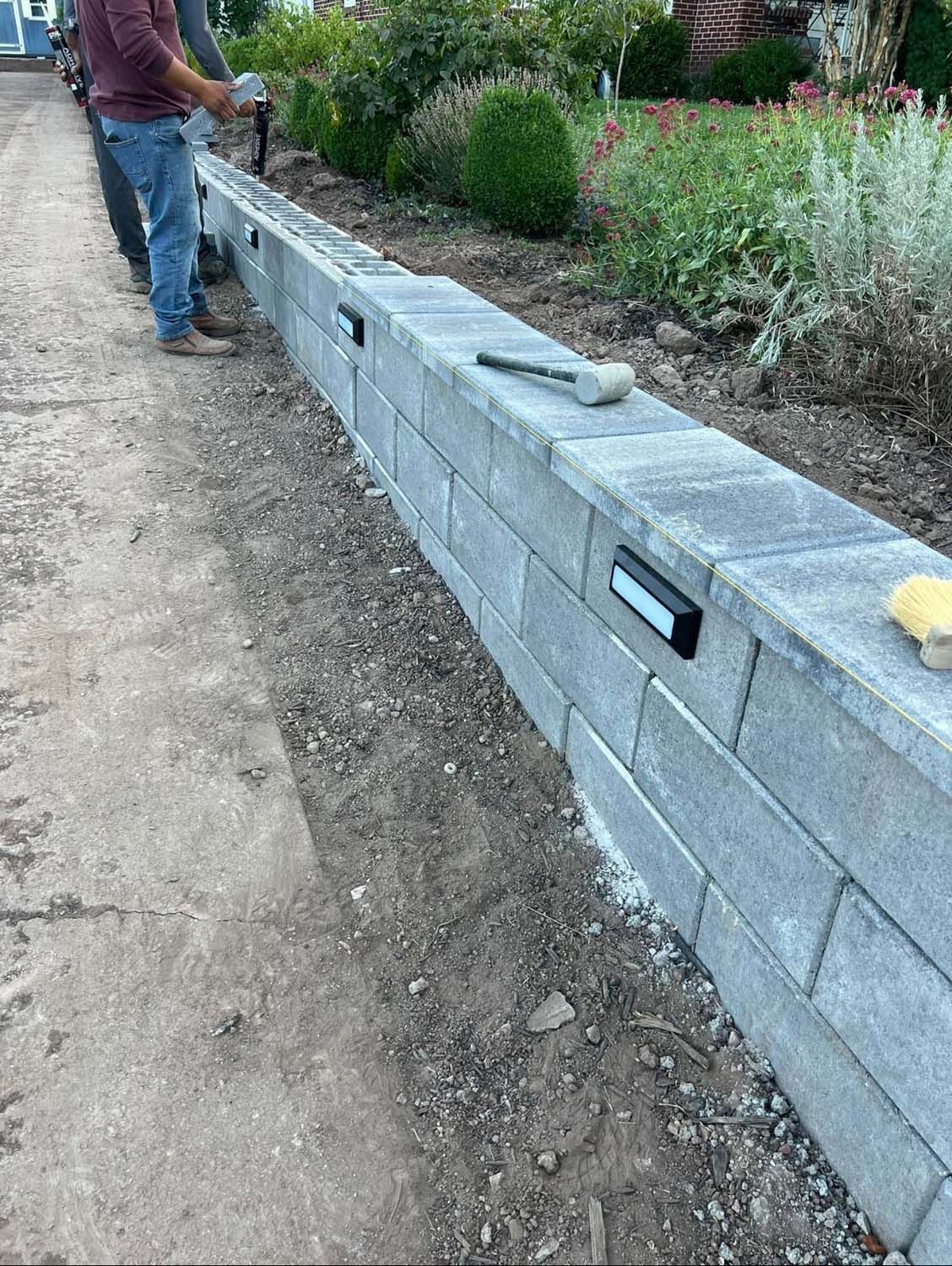 A man is standing next to a brick wall in a garden.