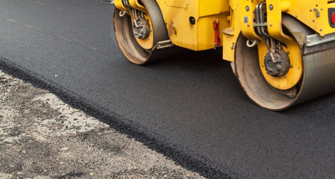 A yellow roller is rolling asphalt on a road.