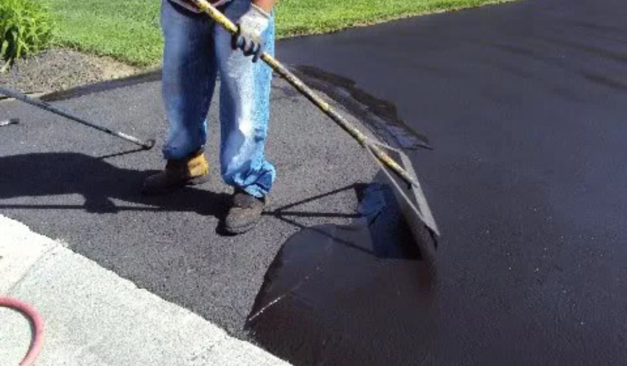 A man is spreading asphalt on a driveway with a shovel.