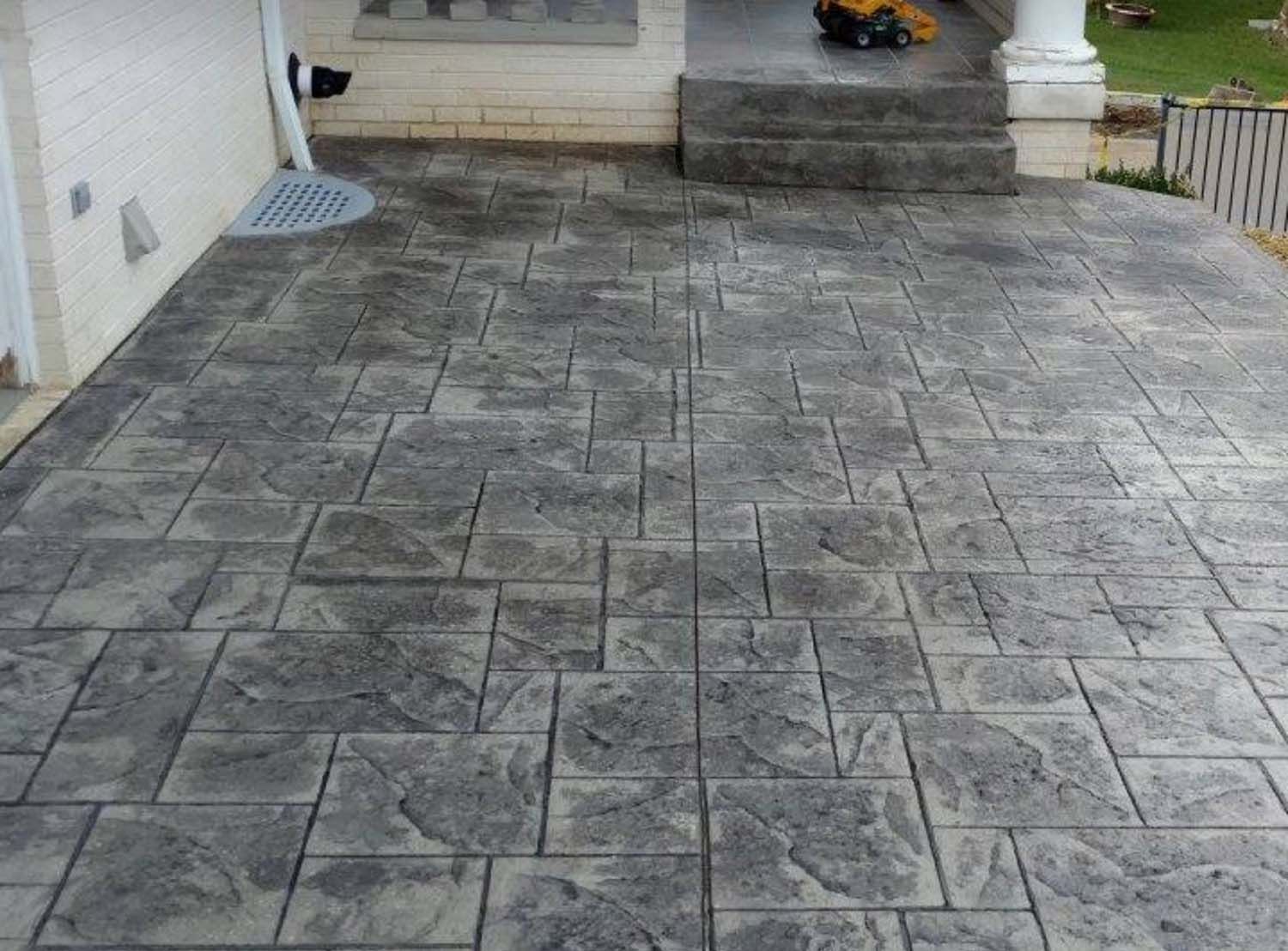 A concrete driveway with a brick pattern and steps leading to a house.