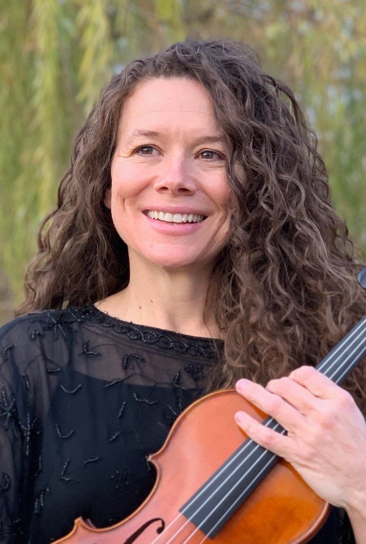 A woman in a green polka dot shirt is holding a violin