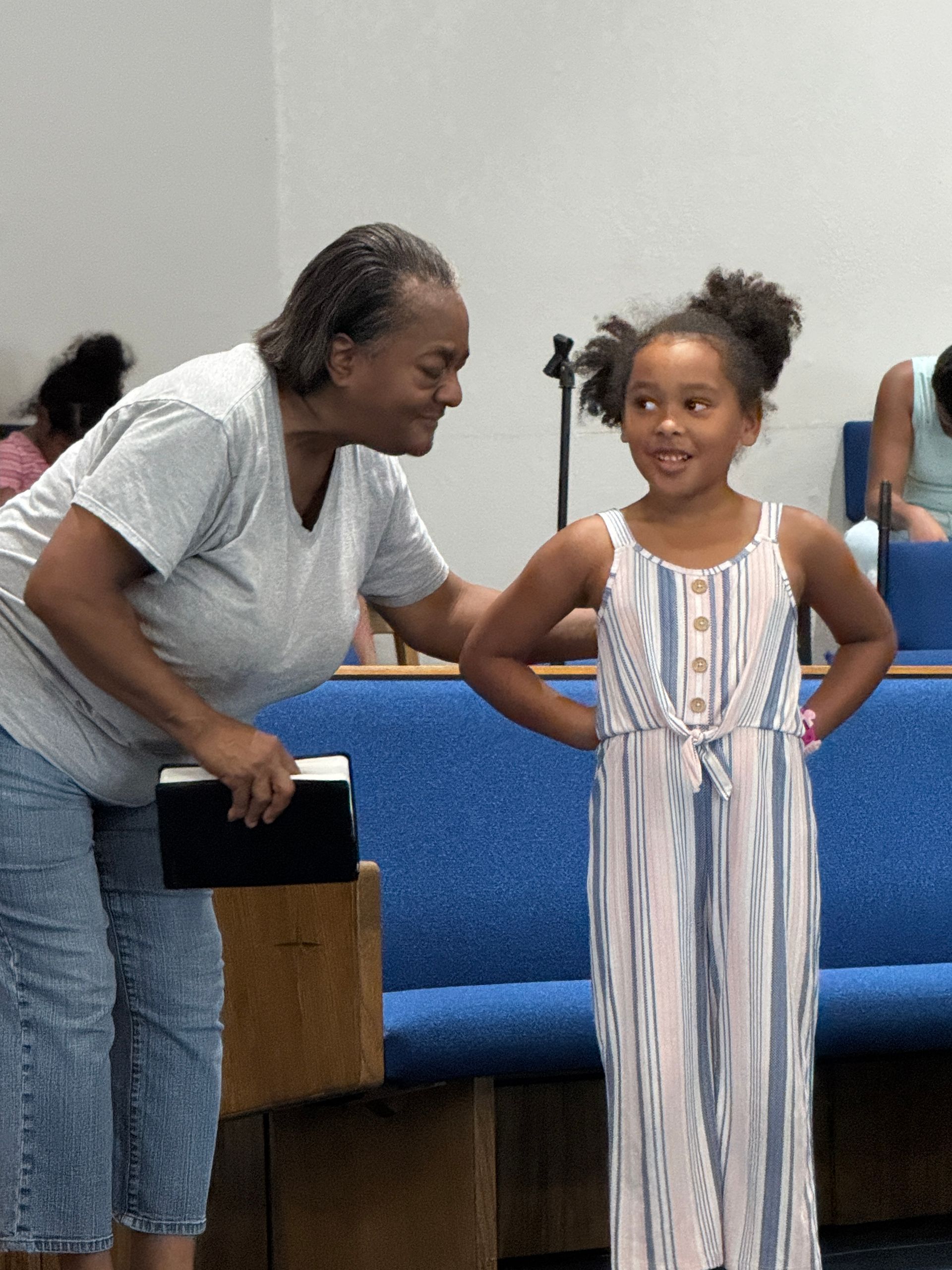 A woman smiles at a young girl in a church. The girl has her hands on her hips.