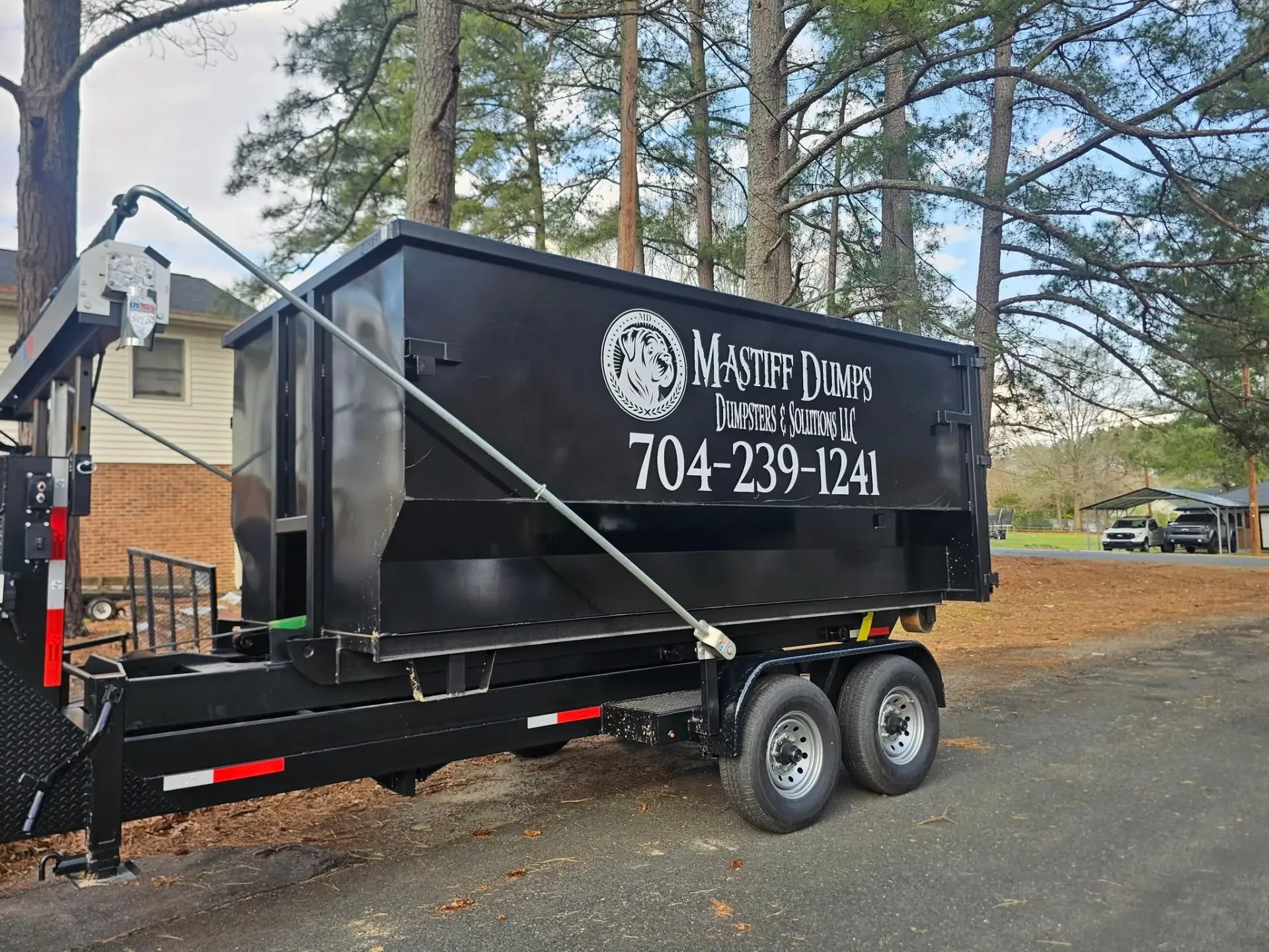 A dumpster trailer is parked in a driveway next to a house.