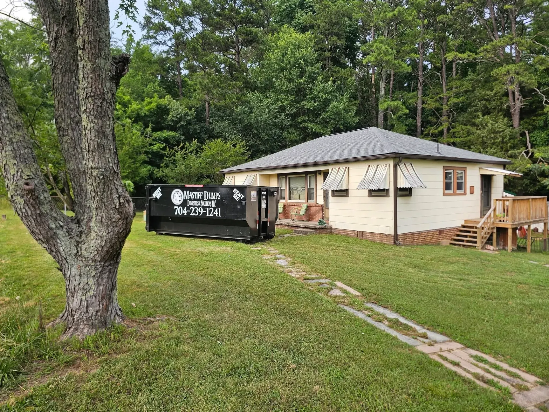 A white house with a black dumpster in front of it in a grassy field.