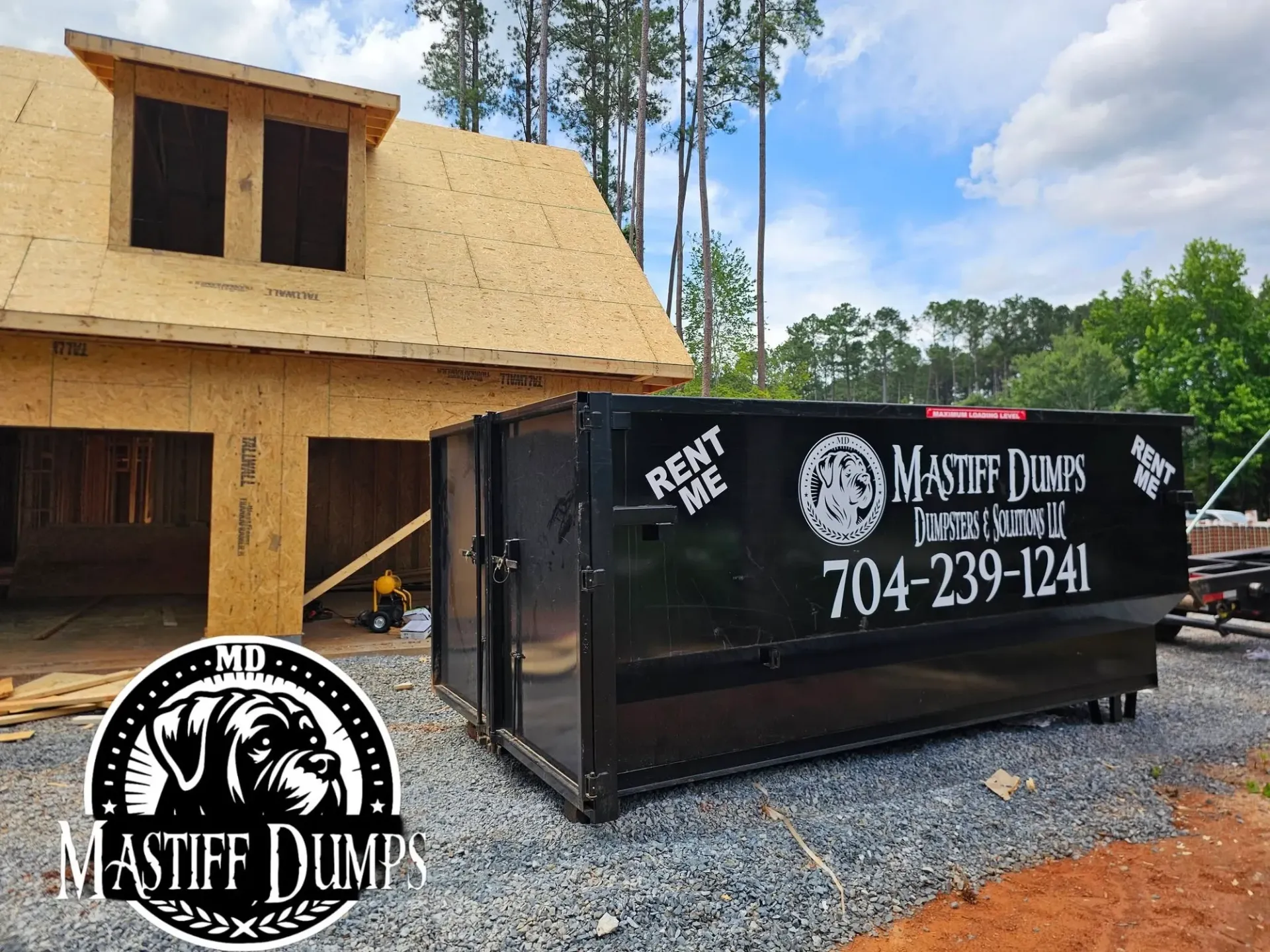 A black dumpster is sitting in front of a house under construction.