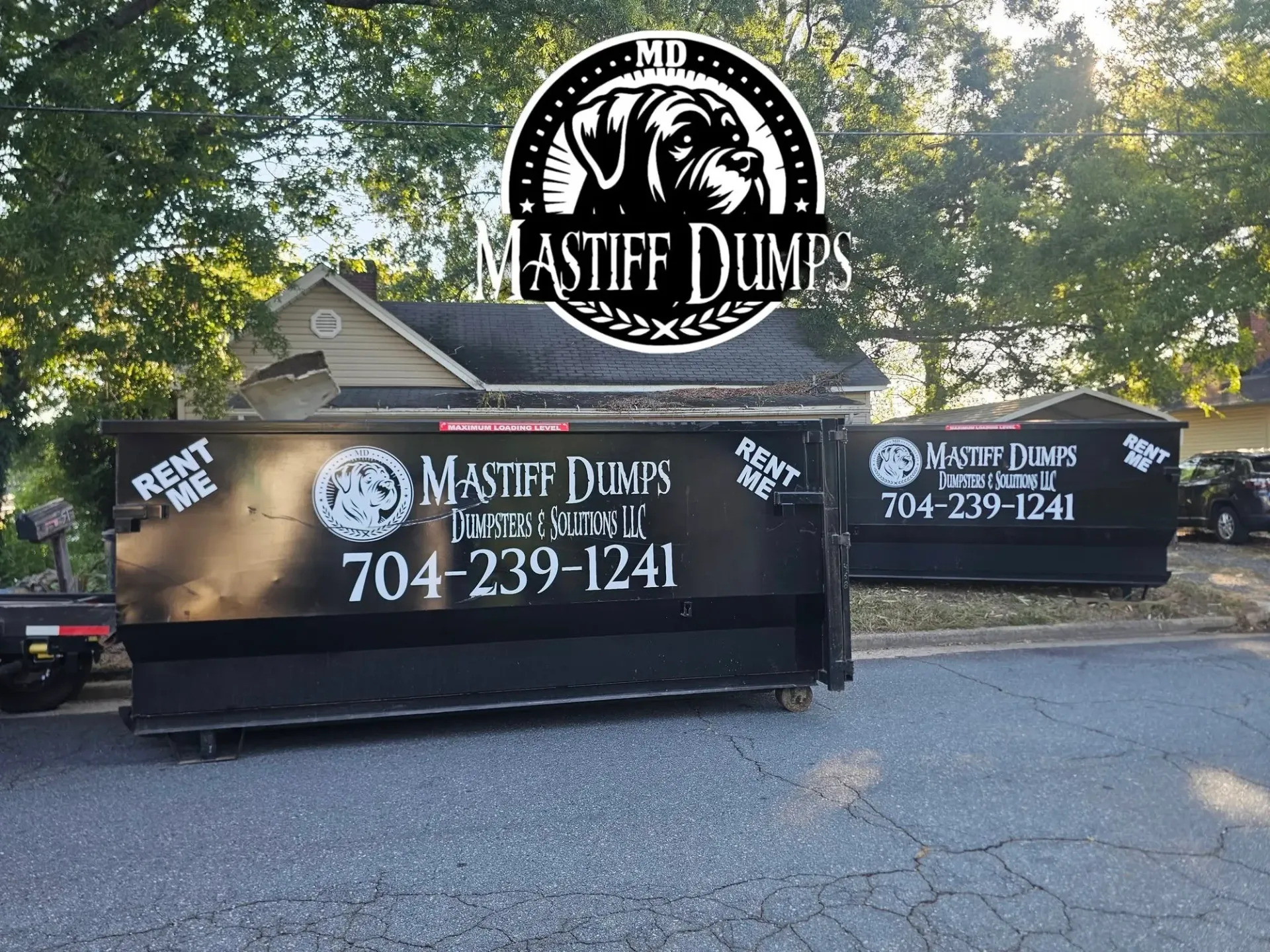 Two dumpsters are parked in front of a house.