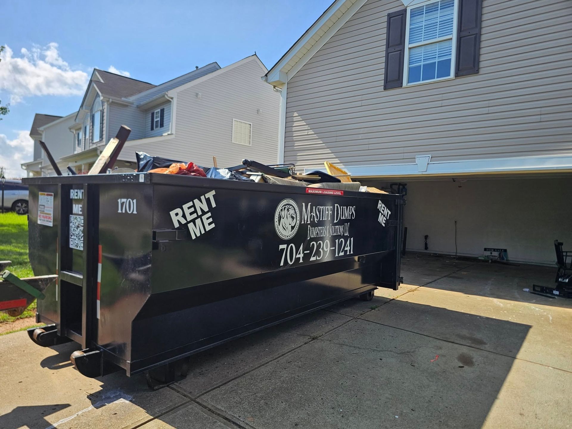 A white house with a black dumpster in front of it in a grassy field.