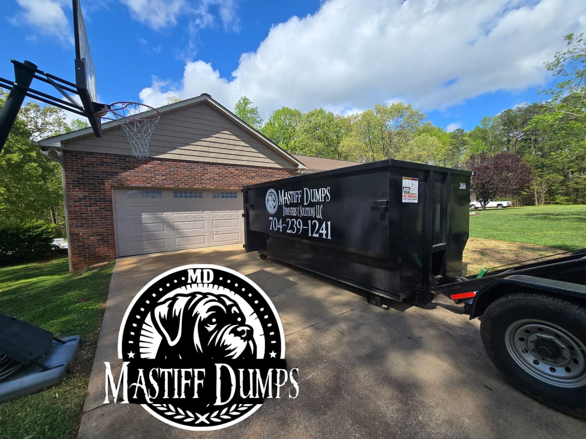 A dumpster trailer is parked in a driveway next to a house.