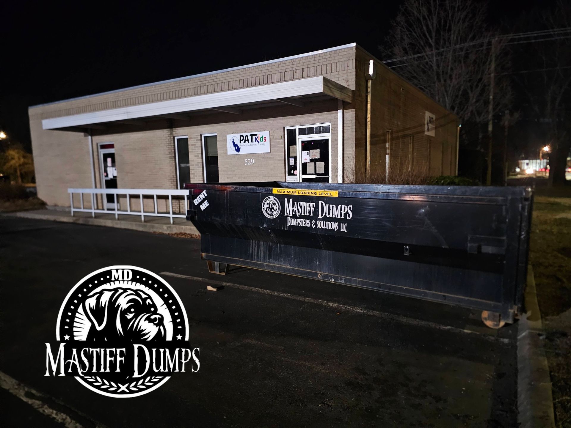 A dumpster is sitting in the grass in front of a building.