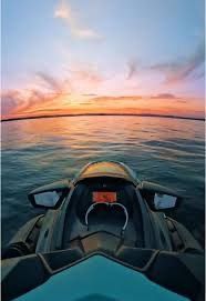 Jet ski on water, facing a sunset. The sky is pink and orange; the water is blue.