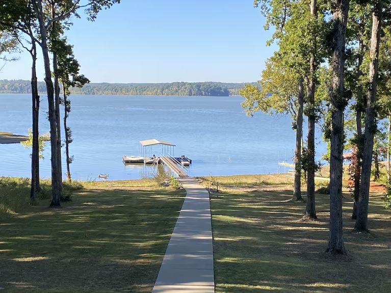 Lakeside view with a dock, grassy lawn, and a path between trees leading to the water.