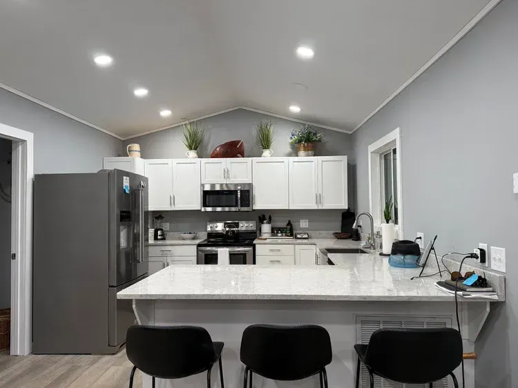 Modern kitchen with gray walls, white cabinets, large island, and three black bar stools
