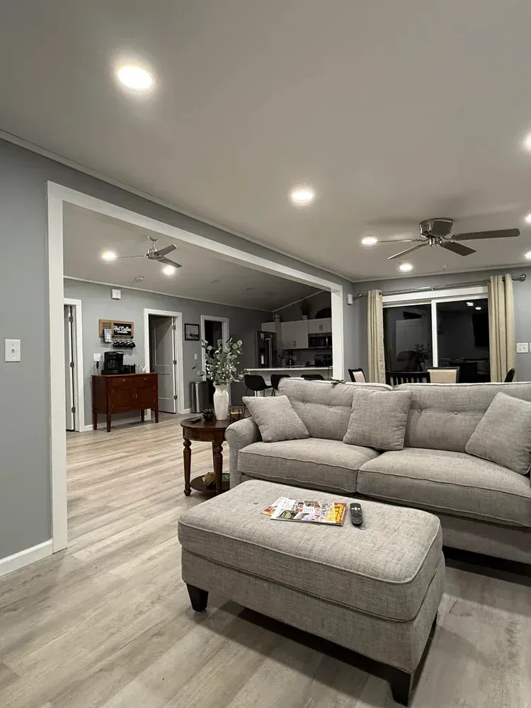 Modern gray living room with sectional sofa, ottoman, recessed lights, and open view to dining area.