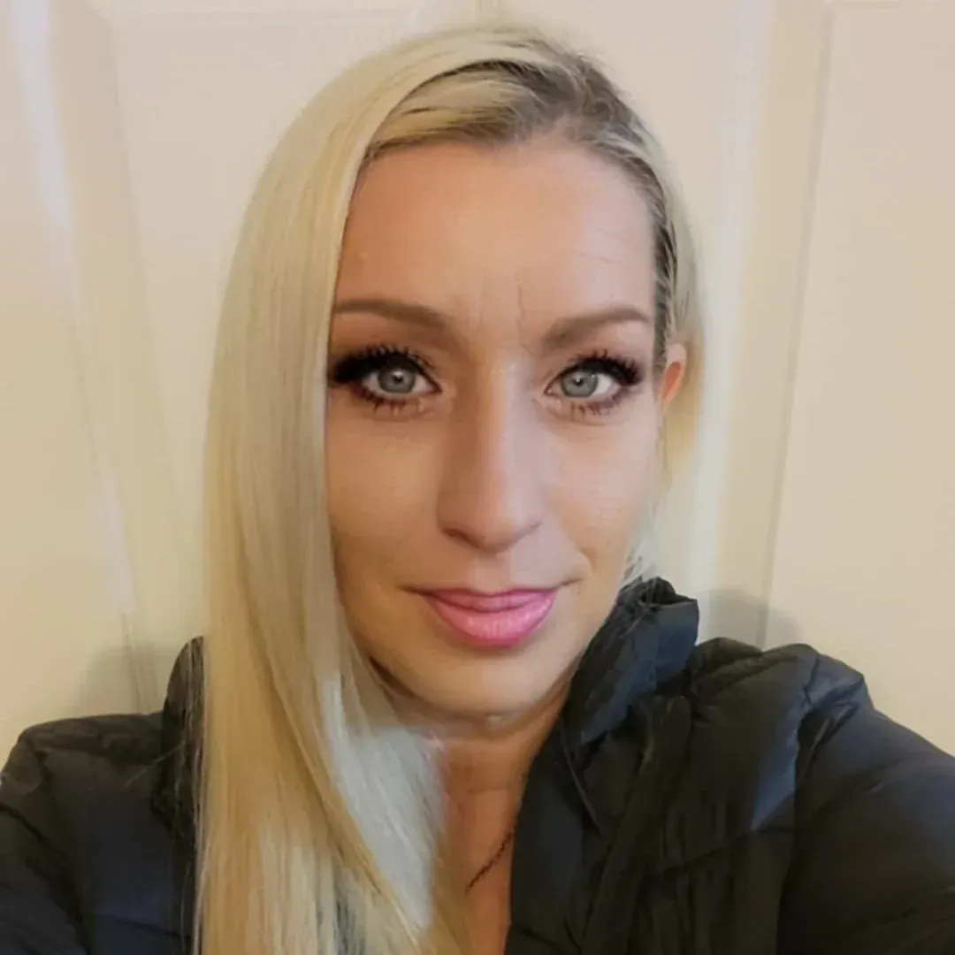 Blonde woman in green sweater smiling at the camera, against a gray background.