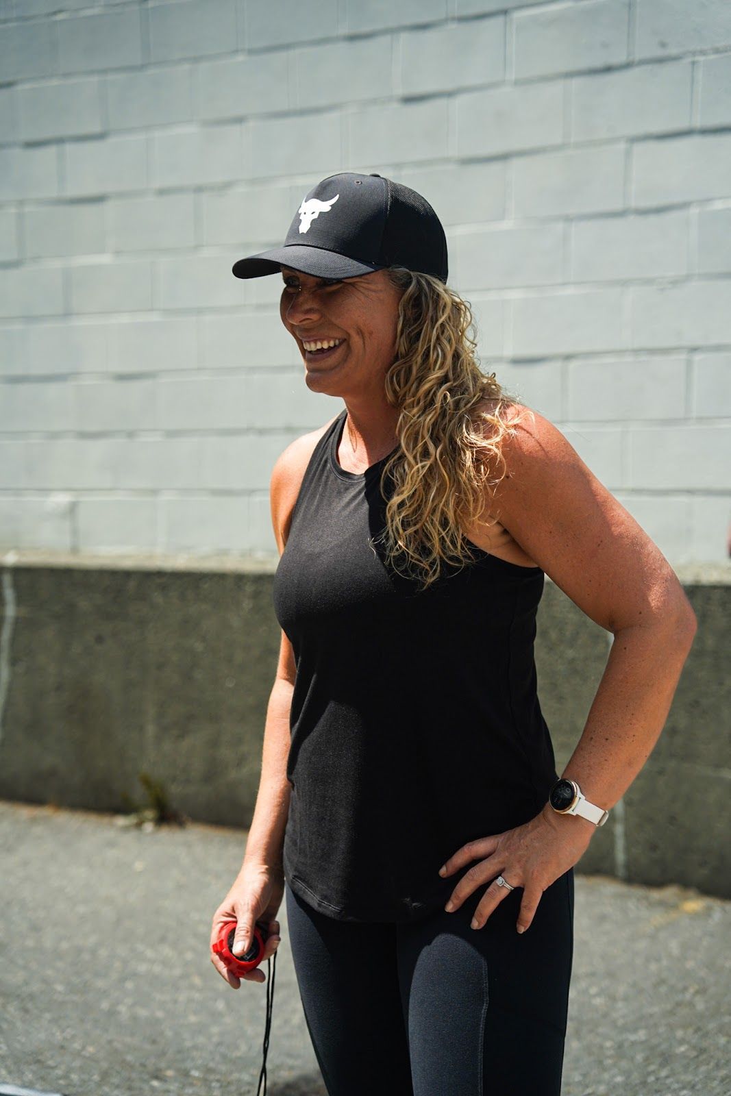 A woman wearing a black tank top and a black hat is standing in front of a brick wall.