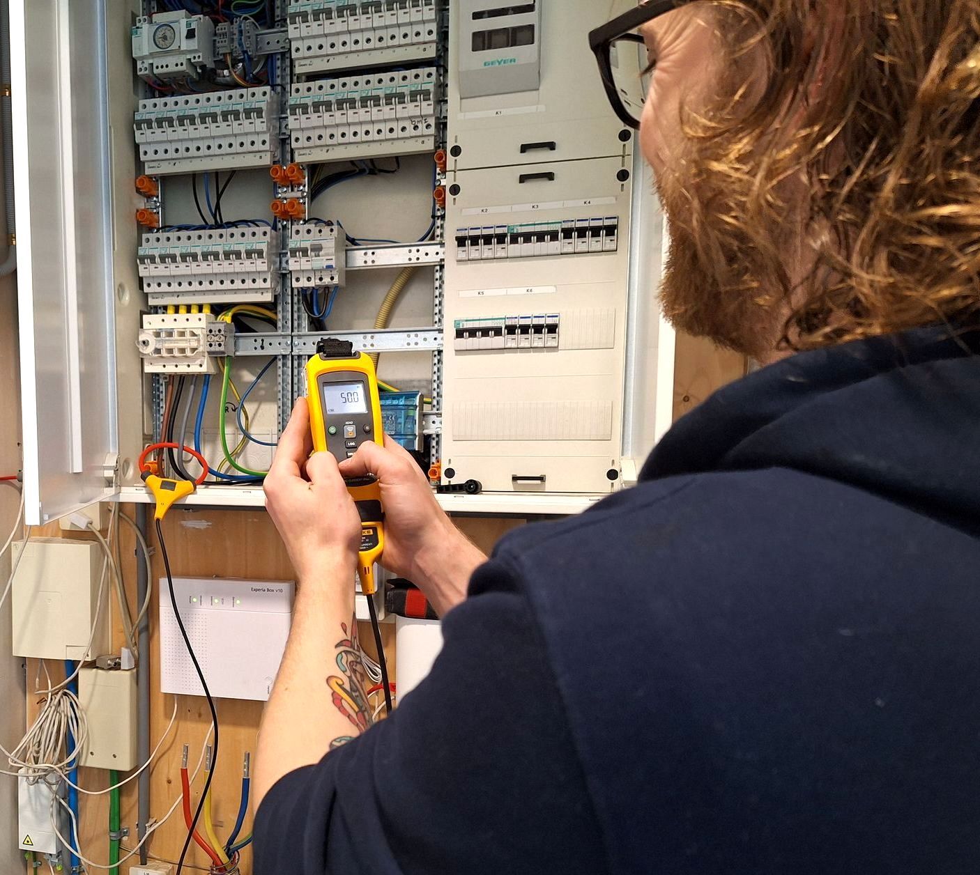Een man in een blauwe hoodie werkt aan een elektrische doos