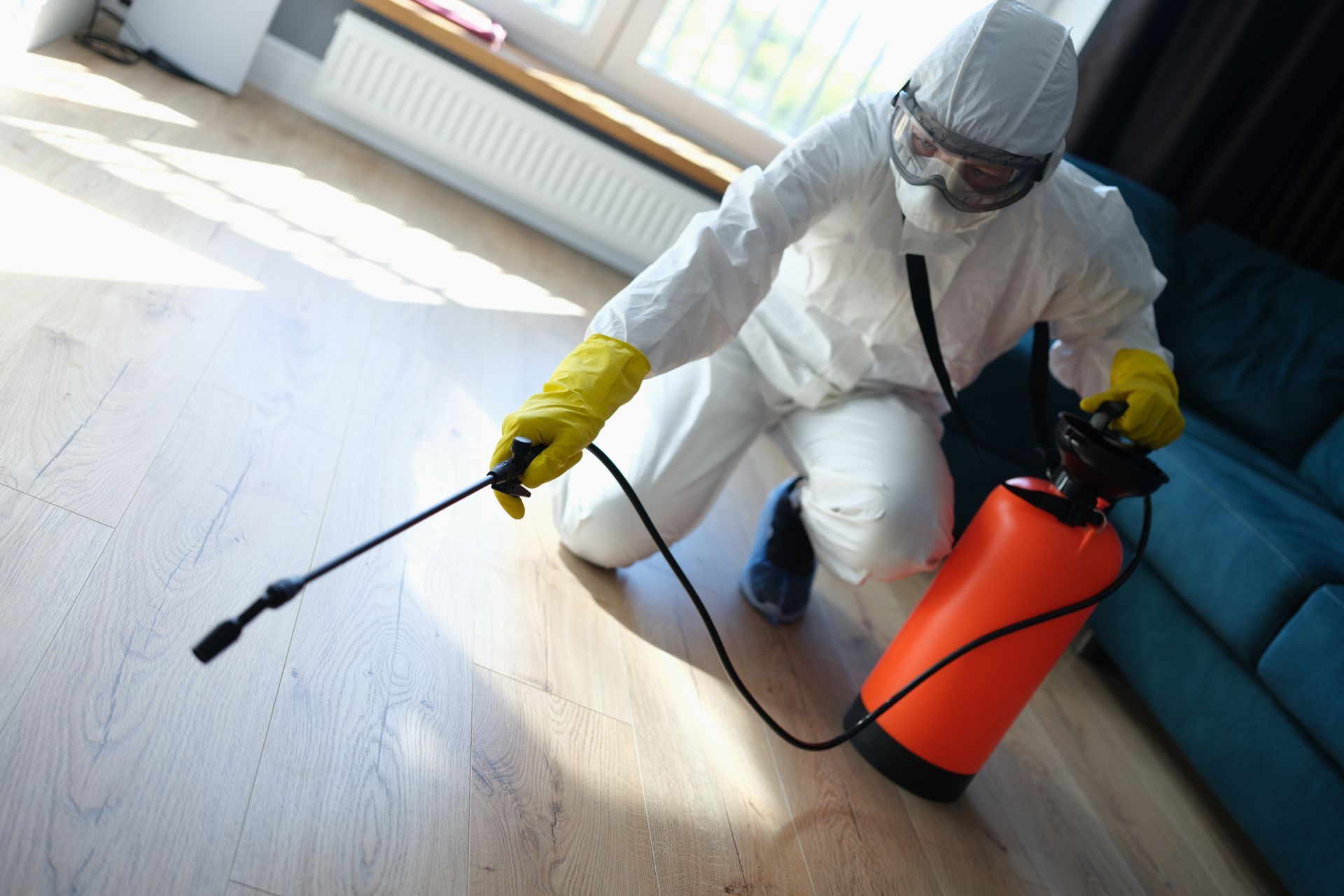 a man in a protective suit is spraying a wooden floor with a sprayer .