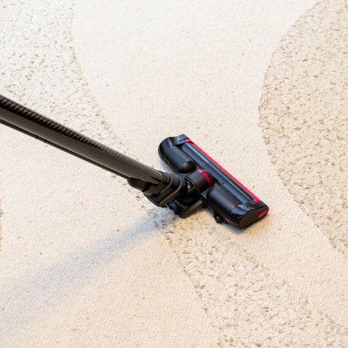 Vacuum cleaner cleaning a white carpet; black and red details.