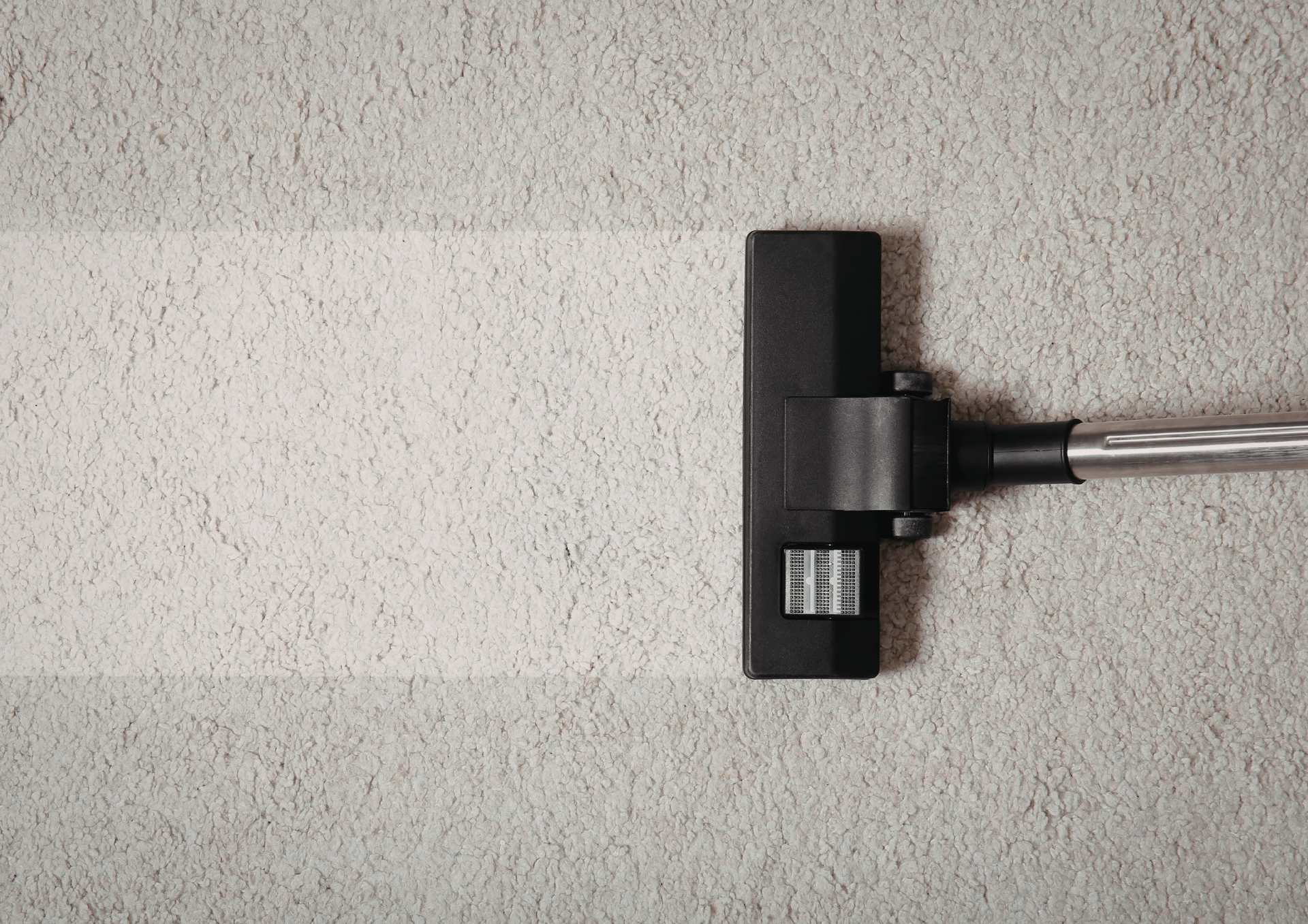 Vacuum cleaner cleaning a light-colored carpet, creating a clean white strip.