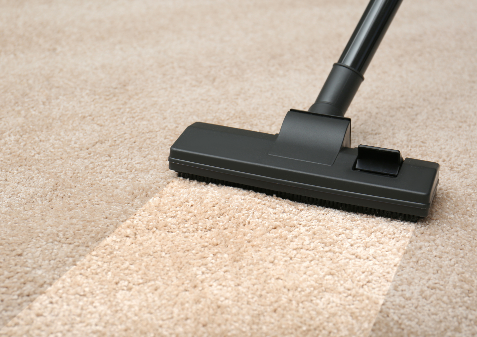 Vacuum cleaner cleaning beige carpet, leaving a clean path.