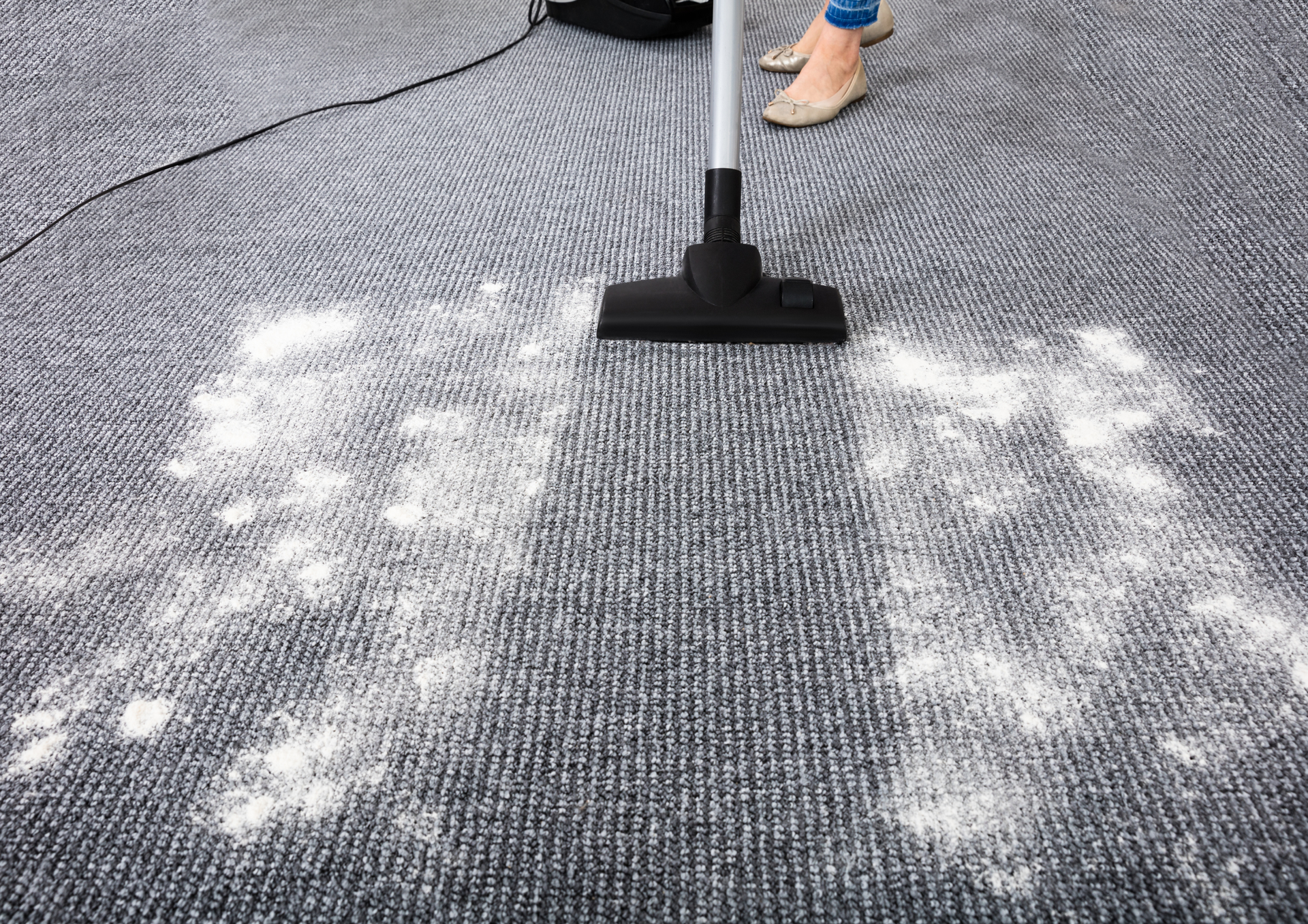 Vacuuming a gray carpet with white residue.