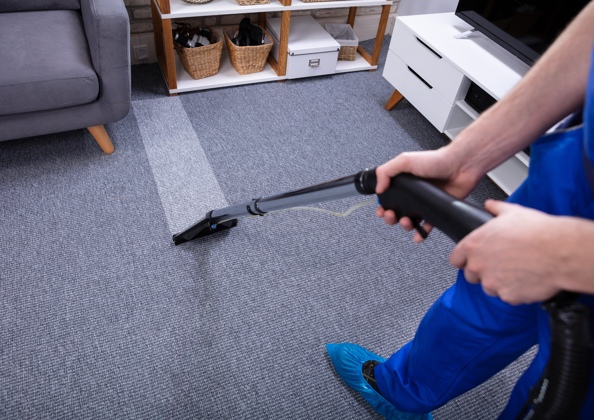 Person in blue suit vacuums a carpet, cleaning a visible path in a living room.
