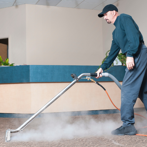 Man using carpet cleaning machine on a beige carpet, creating steam.