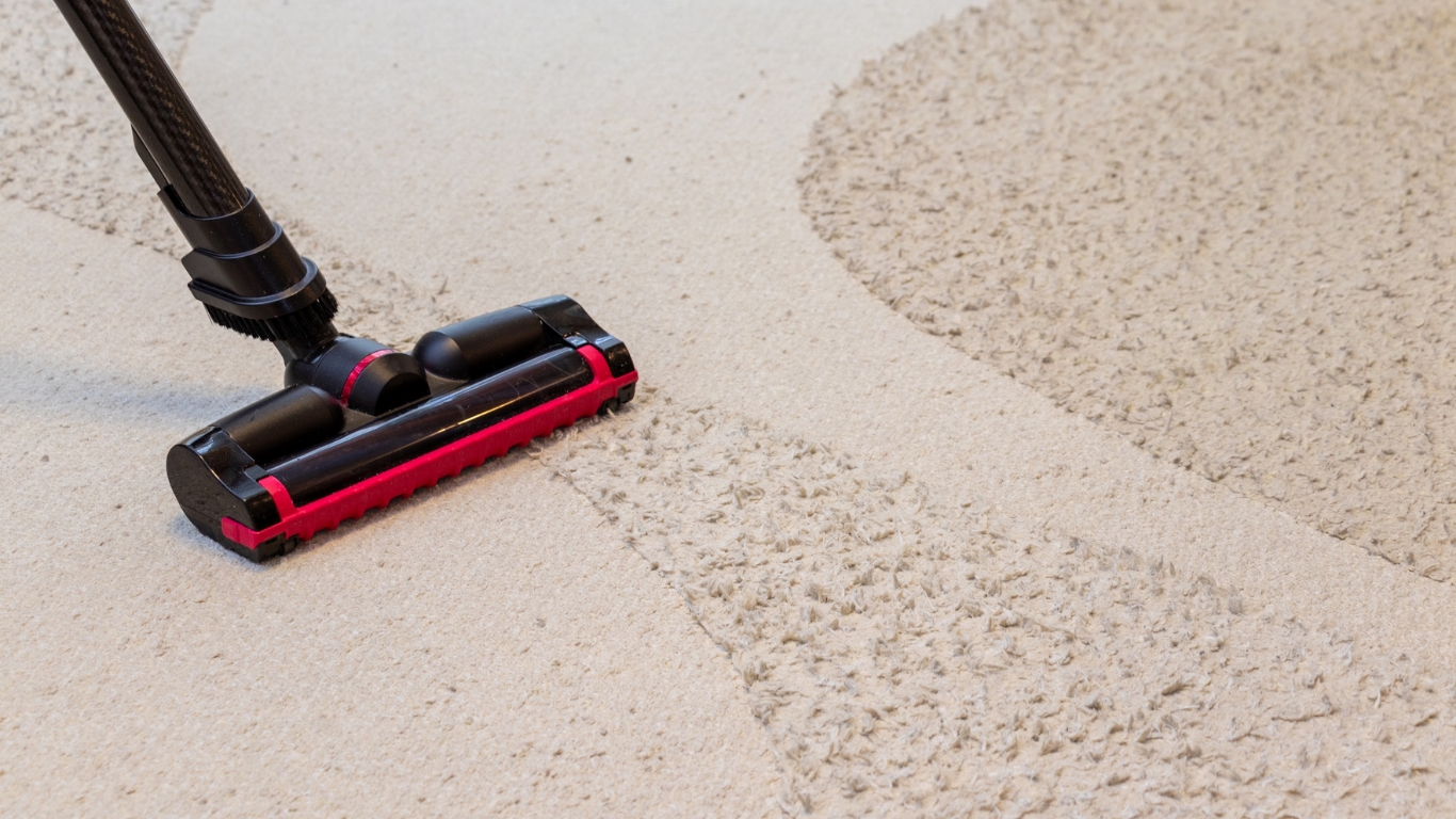 Vacuum cleaner head with red accents cleaning a light-colored rug, leaving a clean trail.