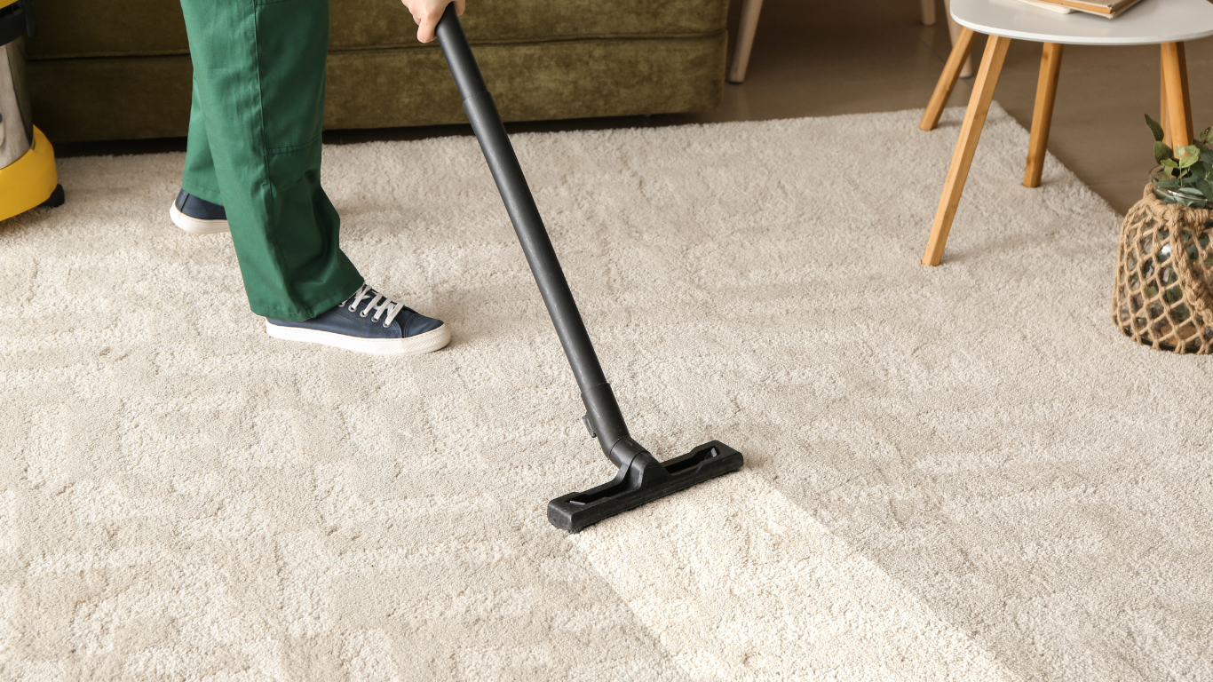 Person vacuuming a cream-colored rug in a living room; visible vacuum path.