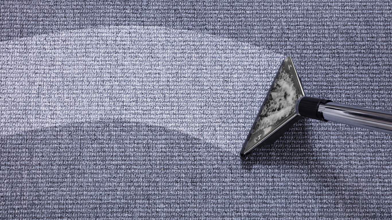 Vacuum head cleaning a textured, blue fabric, creating a lighter path.