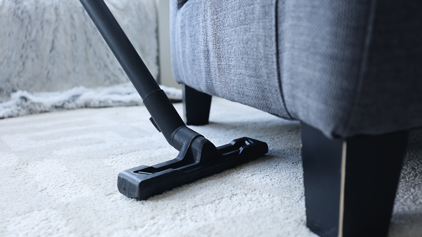 Vacuum cleaner cleaning light-colored carpet near a gray armchair.