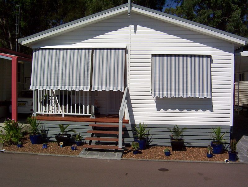 A White House With Striped Awnings On The Windows — Mid Coast Flooring & Blinds In Old Bar, NSW