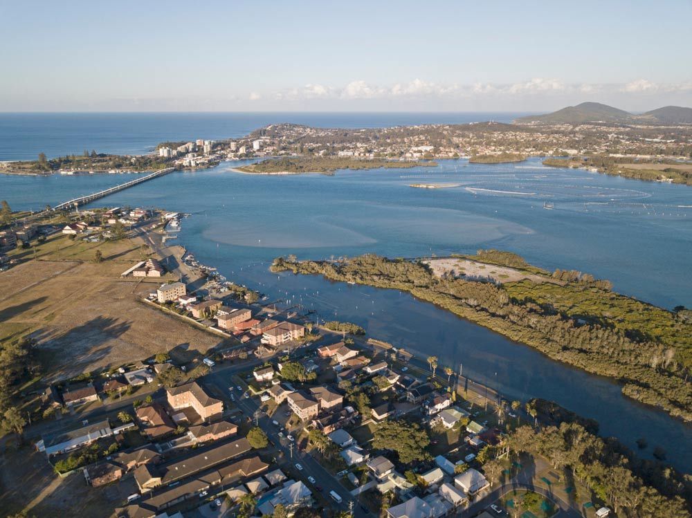 An Aerial View Of A Body Of Water Surrounded By Houses And Trees — Mid Coast Flooring & Blinds In Forster,  NSW