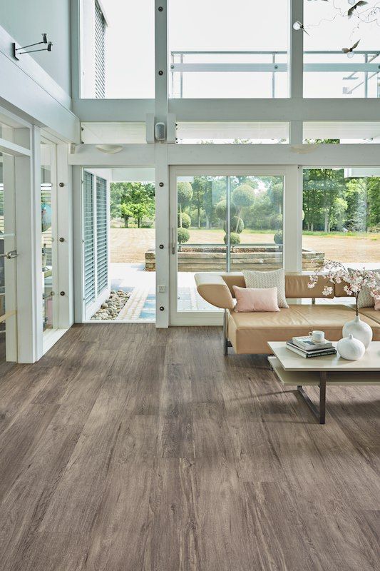 Living room with wood-look flooring, large windows, and a tan sofa overlooking a yard.
