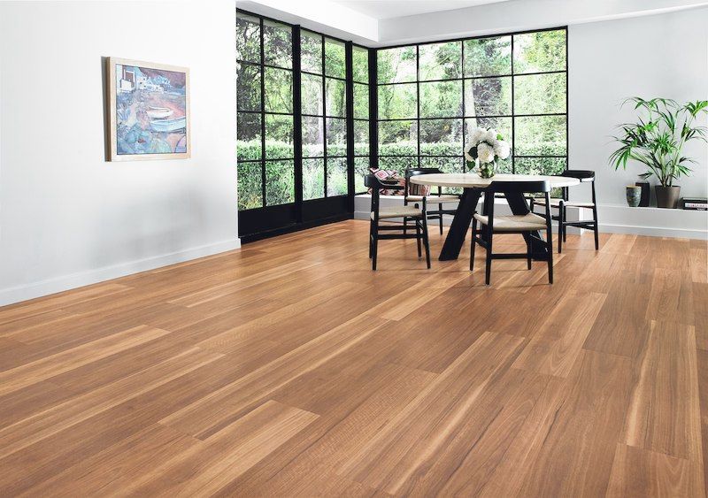 Hardwood floor interior with dining table, chairs, and large windows overlooking greenery.
