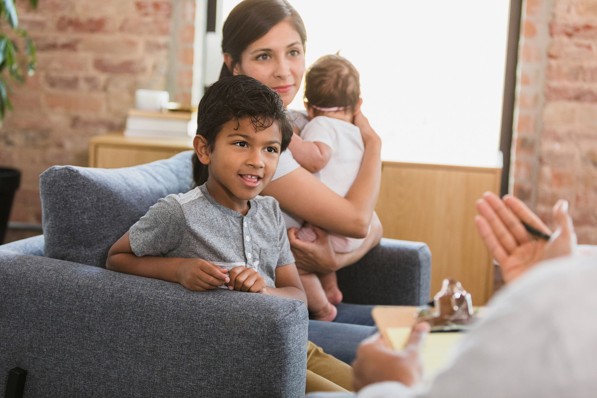 Una donna tiene in braccio un neonato e un bambino mentre è seduta su un divano.
