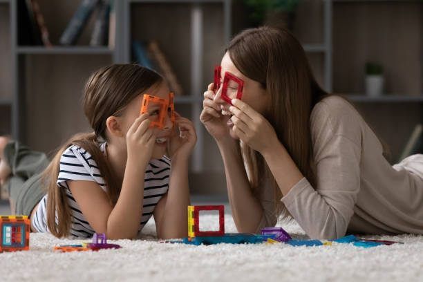 Woman and child lying on a rug, holding colorful shapes up to their eyes.