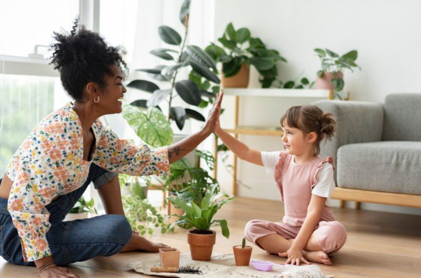 Woman and child high-fiving while gardening indoors, surrounded by plants and pots.