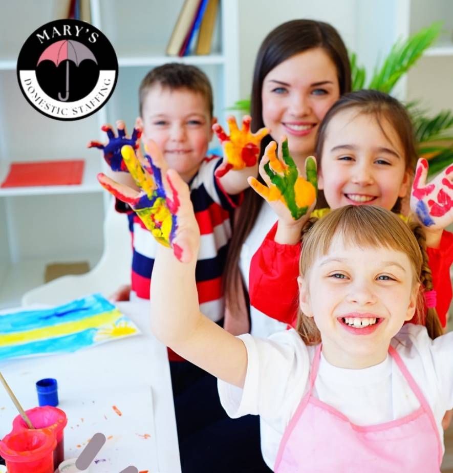 Children and a caregiver show off painted hands in a brightly lit room with craft supplies.